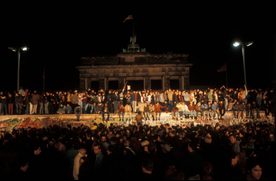 Blick auf die Berliner Mauer mit feiernden Menschen obendrauf