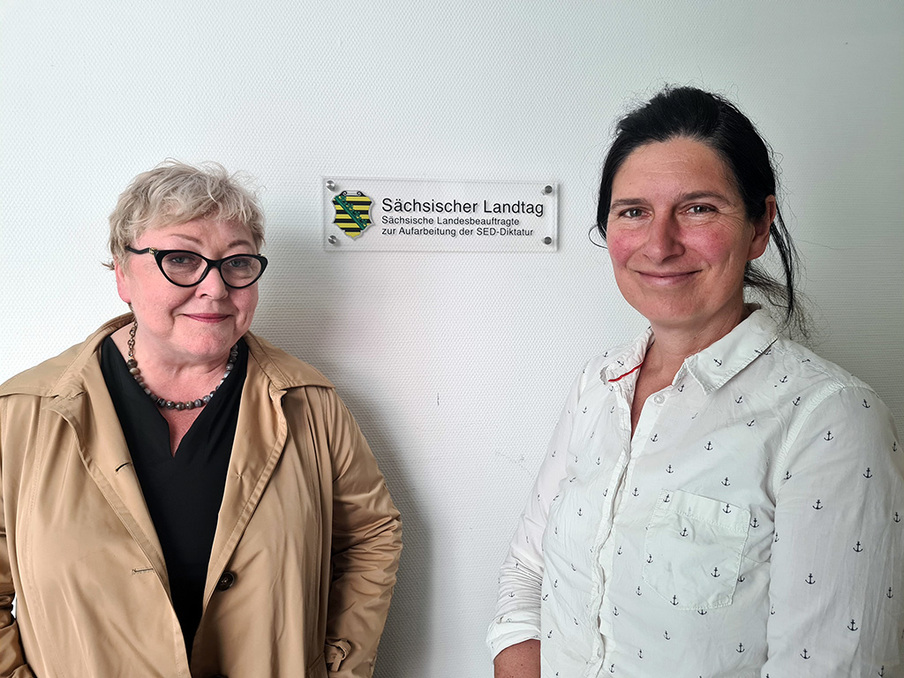 Brustportrait von Zupke und Aris vor Behördenschild in der Mitte